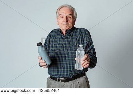 Puzzled senior man holding a reusable and a plastic water bottle