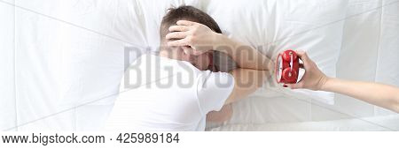Young Man Covers His Ears With His Hands So As Not To Hear Sound Of Alarm Clock