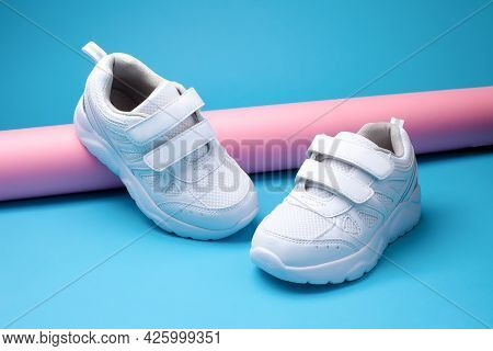 Closeup Two White Woman Sports Shoes On A Pink Long Paper Tube On A Geometric Blue Background In A T