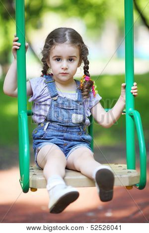 Little girl with pigtails sitting on a swing at the playground