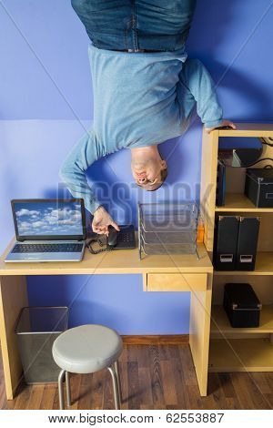 Man in jeans standing on the ceiling under the table with computer
