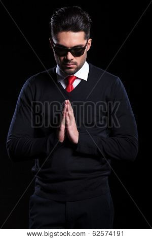 young business man praying with his hands together and looking down. on a black background