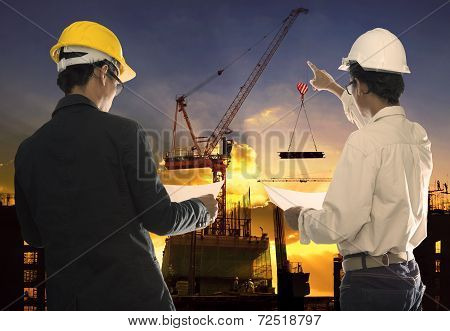 Two Civil Engineer Working In Building Construction Site Against Beautiful Dusky Sky With Crane Cons