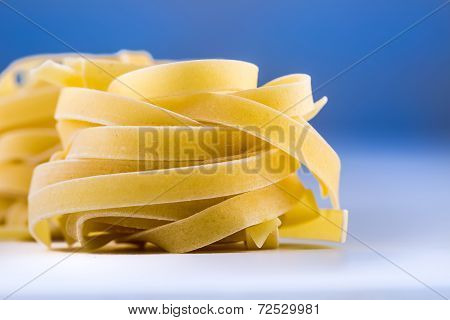 Tagliatelle pasta on white blue background.