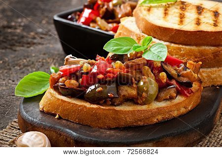 Bruschetta caponata with raisins and pine nuts decorated with a leaf of basil