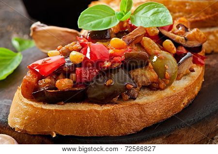Bruschetta caponata with raisins and pine nuts decorated with a leaf of basil