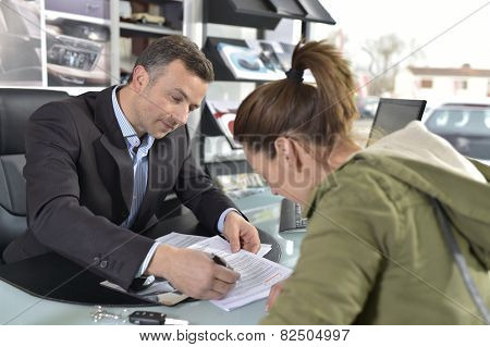 Young woman signing credit contrat for car purchase