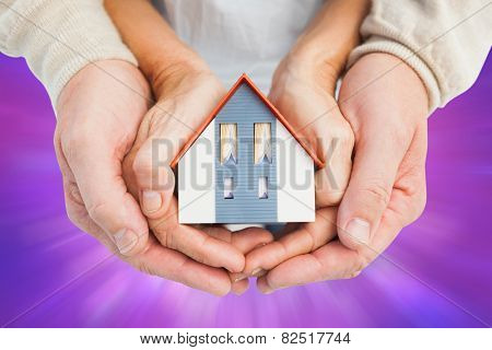 Couple holding small model house in hands against purple abstract light spot design