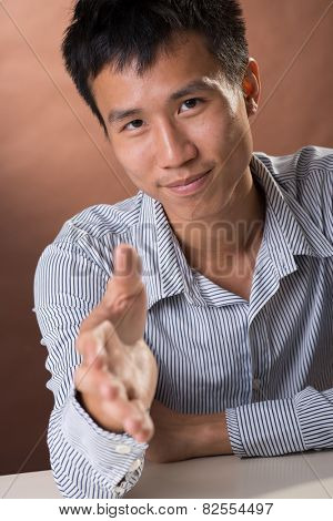 Successful business man of Chinese sitting and want to shake hand with you, closeup portrait in studio.