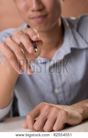 Business man holding pen and pointing at you.