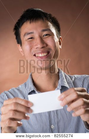 Young Chinese frank businessman holding blank white business card, closeup portrait in studio.