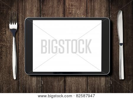 black tablet pc or ipad on dark wooden table with fork and knife