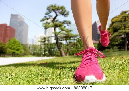 Running shoes - woman runner jogging staying fit in Tokyo Park, Japan. Closeup of pink trainers in green grass in summer park near the Imperial Palace and Ginza district downtown.
