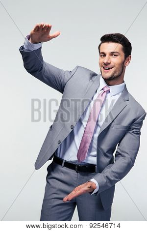Happy businessman bragging about the size of something over gray background. Looking at camera