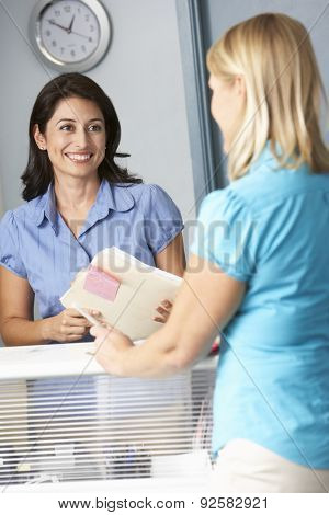Female Patient With Receptionist In Doctors Waiting Room