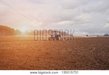 In the earlyspring morningbecause of the wood the bright sun ascends.The tractor goes and pulls a plowplowing a field before landing of crops.On the earth dry stalks of a last year's sunflower lie.