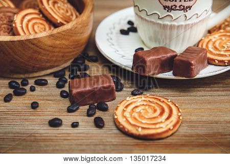 There are Cookies,Candy,Chocolate Peas,Poppy;Porcelain Saucer and Cap with Coffe,Tasty Sweet Food on the Wooden Background.Toned