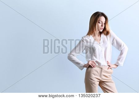 Beautiful young woman in a white shirt and beige pants on blue wall background