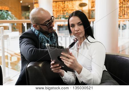 Arab man and stylish girl looking photos on digital tablet in shopping centre