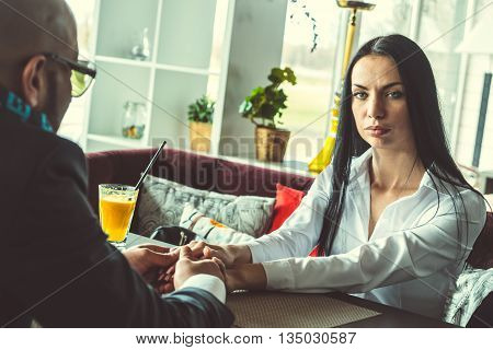 Arab man and the stylish girl sitting and holding hands in the restaurant
