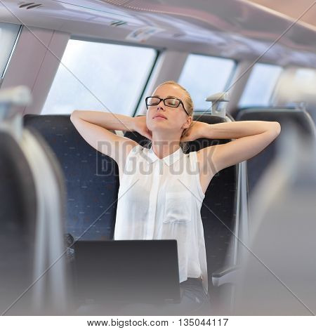 Businesswoman traveling by train, streching on her seat while working on laptop. Business travel concept.