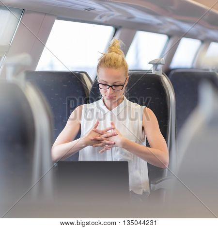 Businesswoman traveling by train, streching her fingers on her seat while working on laptop. Business travel concept.
