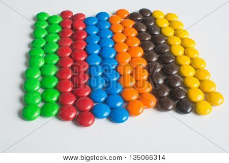 Pile of colorful chocolate bonbon candies sorted and organised into rows on white background