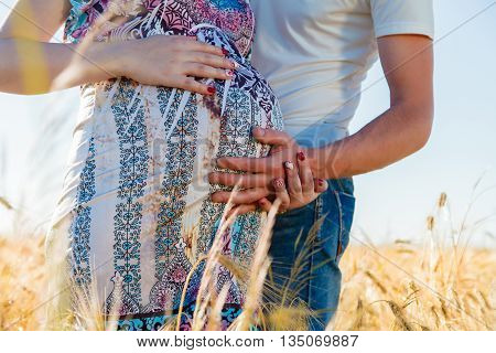 Happy and young pregnant couple hugging in nature