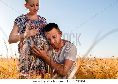 Happy and young pregnant couple hugging in nature
