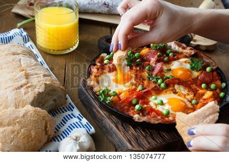 Hand dip bread into flamenco eggs or huevos a la flamenca, spanish andalusian cuisine.