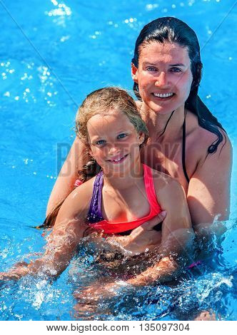 Mother learn her daughter swiming in swimming pool. Mother hugging daughter. Happy family have healthy lifestyle in swimming pool.