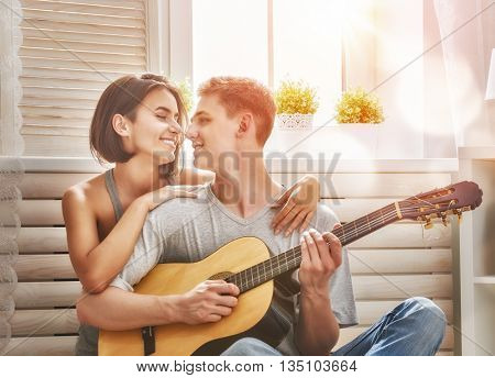 Happy couple in love. Stunning sensual portrait of young stylish fashion couple indoors. Young man playing guitar for his beloved girl.