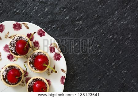 Delicious chocolate tartlets with one cherry, chocolate and coconut on slate background