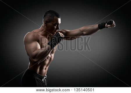 Fighter boxer standing staring strong on black background. Young masculine caucasian male athlete.