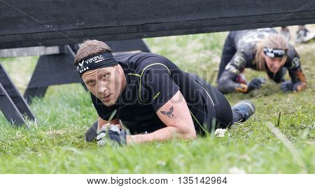 STOCKHOLM SWEDEN - MAY 14 2016: Concentrated man with tatoo crawling below a barb wire obstacle a woman behind in the obstacle race Tough Viking Event in Sweden May 14 2016