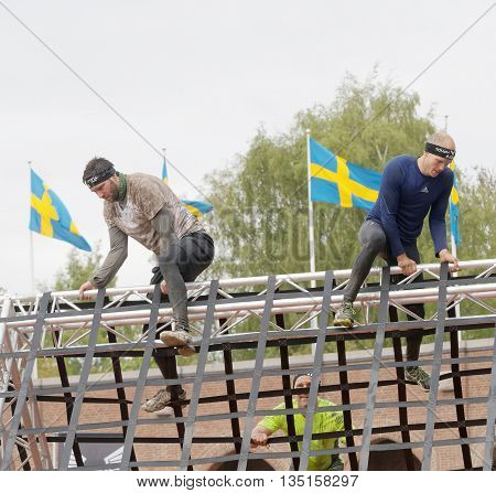 STOCKHOLM SWEDEN - MAY 14 2016: Men climbing a net obstacle swedish flags in the background in the obstacle race Tough Viking Event in Sweden May 14 2016