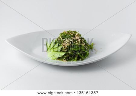 Thai dish of seaweed with sesame seeds and cucumber on a white plate on a white background