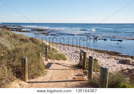 KALBARRI,WA,AUSTRALIA-APRIL 21,2016: Tourists wading in the Indian Ocean waters with dune path and clear skies in Kalbarri, Western Australia.