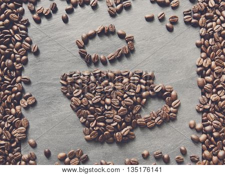 Cup from coffee beans. Heap of roasted coffee bean on grey stone surface texture. Coffee shop or cafe background. Natural stone and cup from beans. Soft color toning, top view
