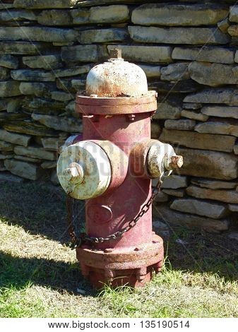 vintage fire plug in the grass next to a stone wall.
