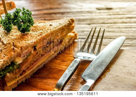 Club sandwich on the wood plate decorate together with fork and knight on the bark wood table background