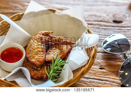 Fried chicken wing in the basket with chilli dipping sauce on the brown bark background decorated with sunglasses