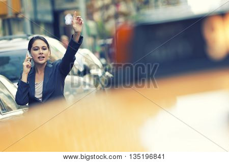 A young woman or businesswoman hailing a yellow taxi cab while talking on her cell phone in a New York City