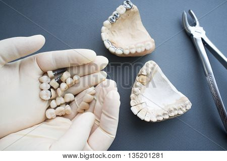 Jaw layout modeling top view. Picking up necessary dentures for plaster jaws.Flat lay of dentures and dental crowns in dentist hands, two plaster jaws and bone forceps