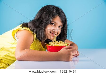 Happy Asian child eating delicious noodle, small indian girl eating noodles in red bowl with chopsticks, over blue background