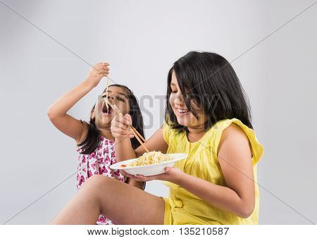 Happy Asian children eating delicious noodle, two cheerful little indian girls eating noodles in white dish isolated over white background