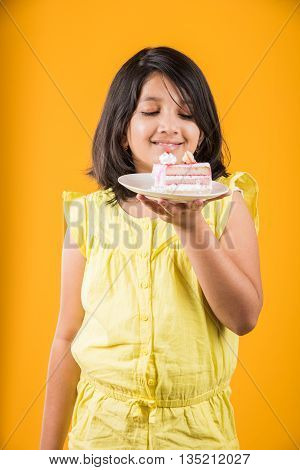 portrait of Indian kid eating cake or pastry, cute little girl eating cake, girl eating strawberry cake or pastry over yellow background