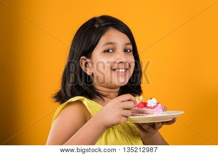 portrait of Indian kid eating cake or pastry, cute little girl eating cake, girl eating cake over colourful background