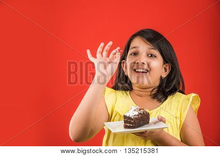 portrait of Indian kid eating cake or pastry, cute little girl eating cake, girl eating cake over colourful background