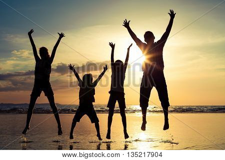 Father and children playing on the beach at the sunset time. Family having fun on the sea. Concept of friendly family and of summer vacation.